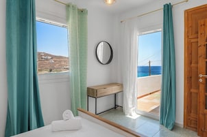 Un dormitorio con cama, una mesita, un espejo y vista al mar.
