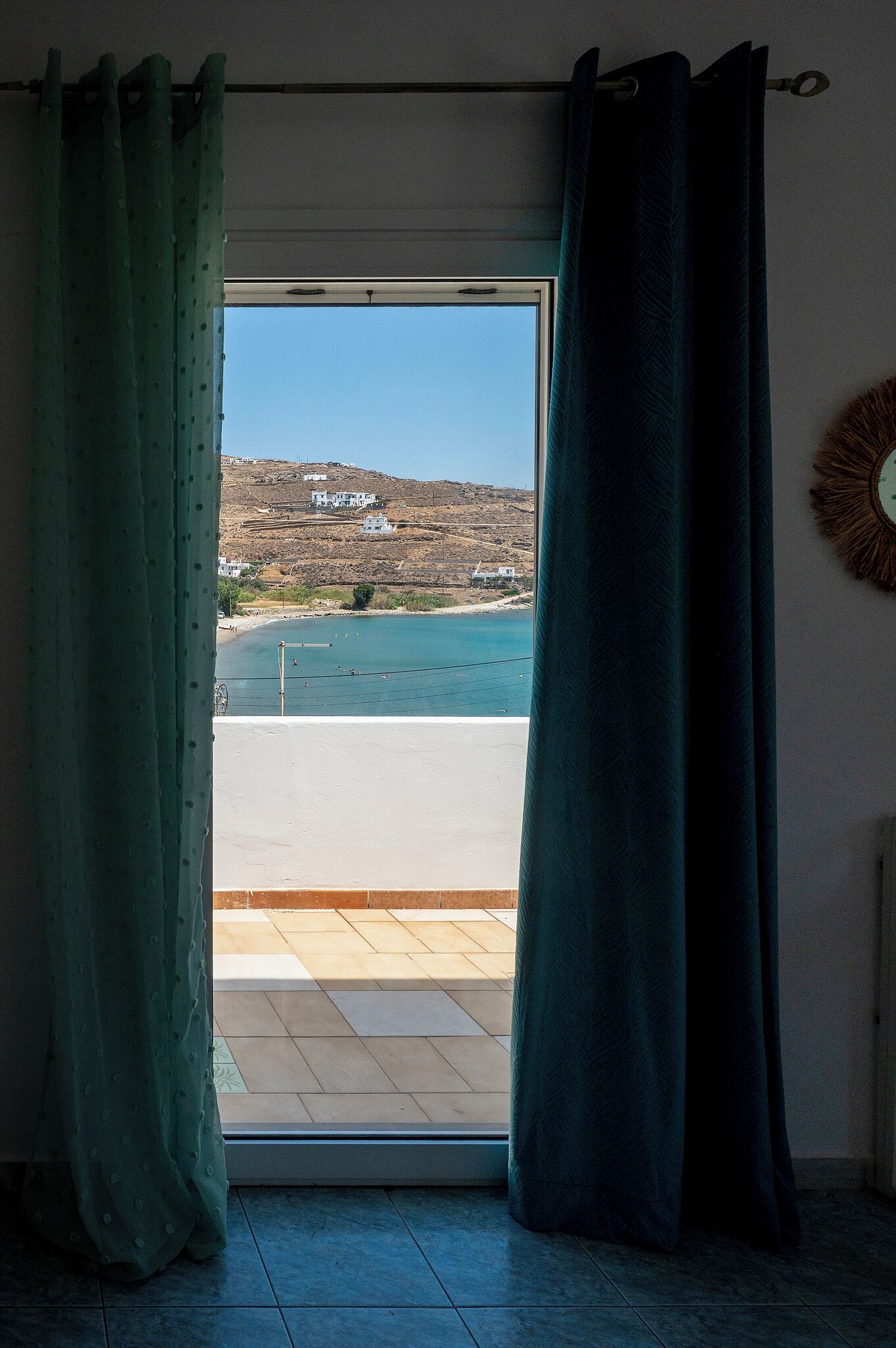 A room with a view of a coastal landscape through a window with green curtains.