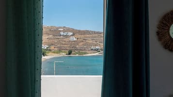 A room with a view of a coastal landscape through a window with green curtains.