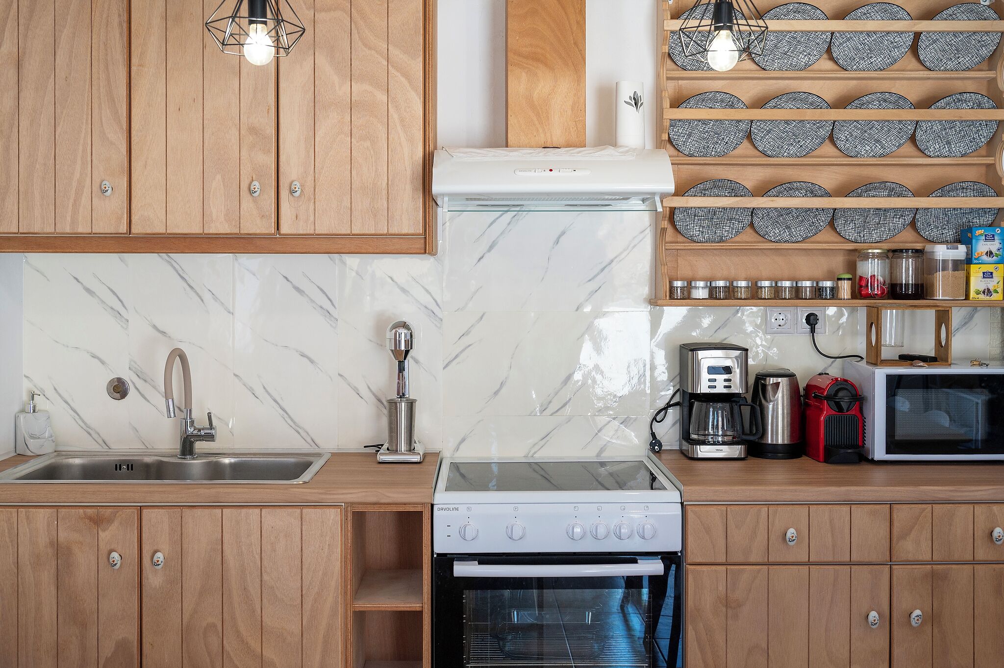 A kitchen with wooden cabinets, a marble backsplash, a stainless steel sink, a coffee maker, a toaster, and a microwave.