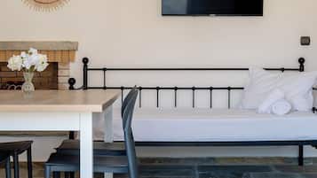 A room with a bed, a TV mounted on the wall, a dining table with chairs, and a decorative mirror.