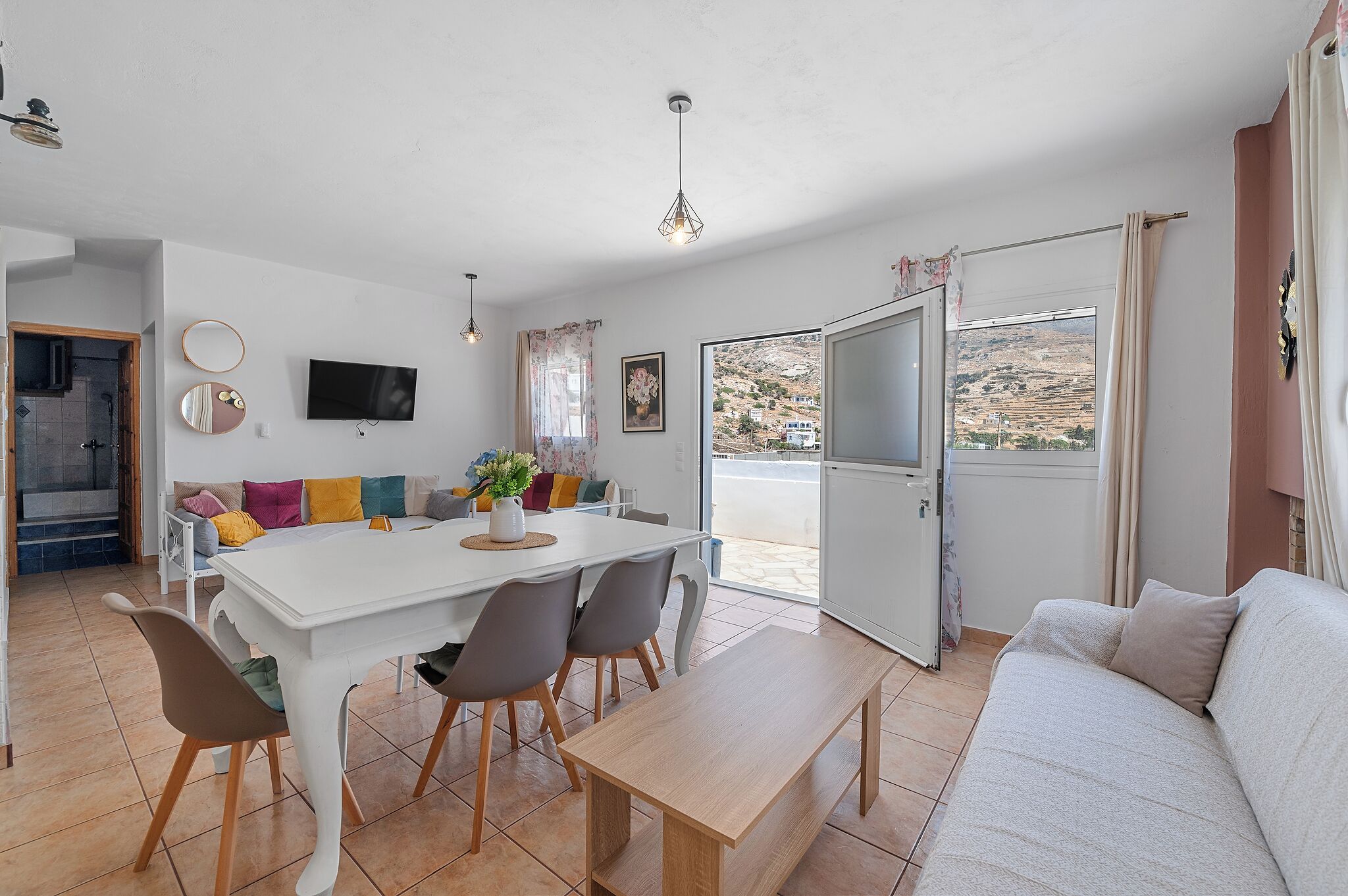 Una sala moderna con comedor, un sofá, un televisor y vistas al exterior.
