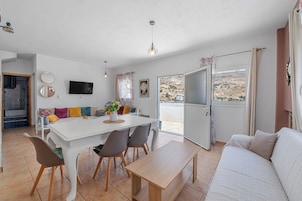 A modern living room with a dining area, a sofa, a TV, and a view of the outdoors.
