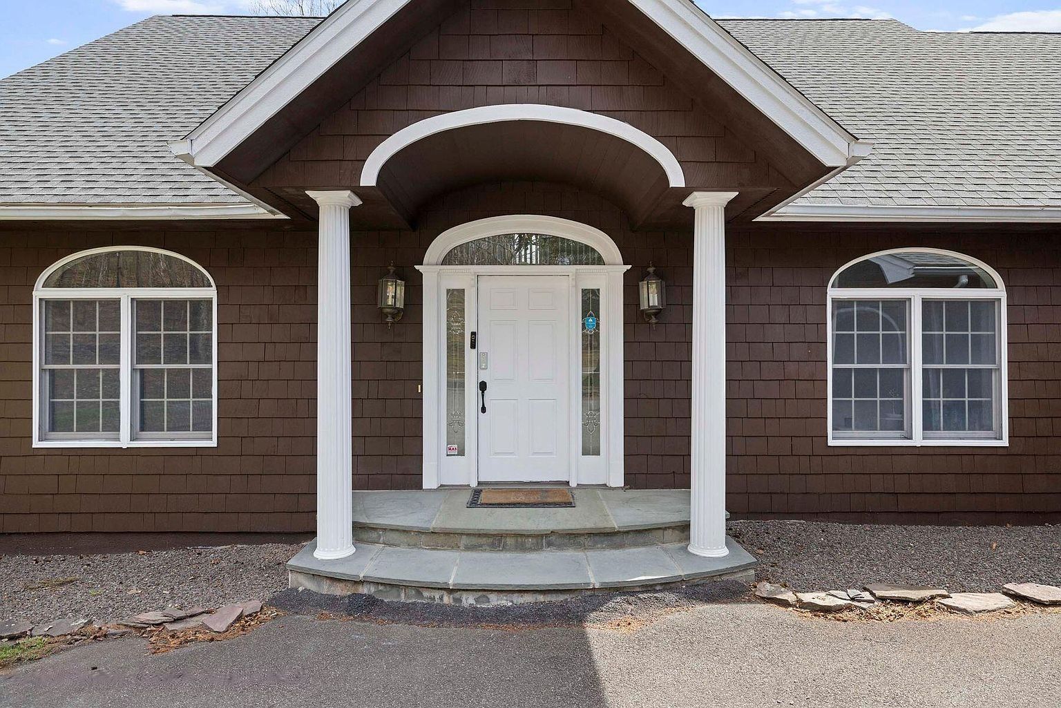 A two-story house with a brown exterior, white trim, and a front porch with a white door.