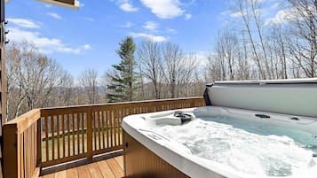 A hot tub on a wooden deck with a view of trees and a clear sky.