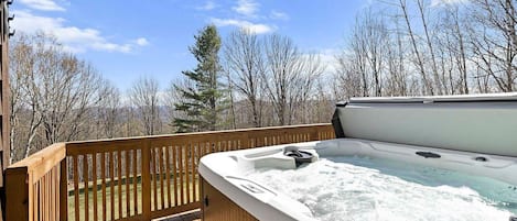 A hot tub on a wooden deck with a view of trees and a clear sky.