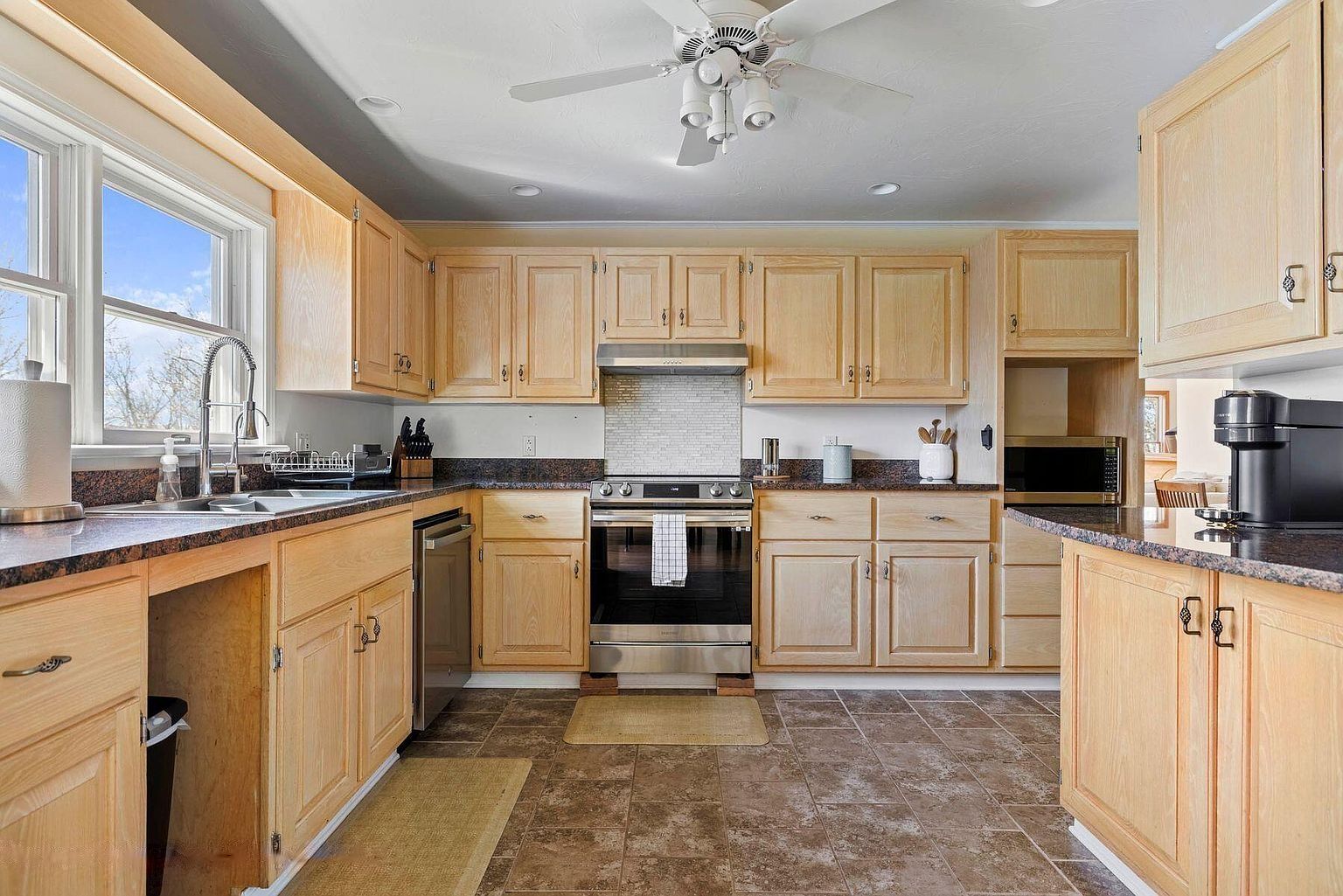 A kitchen with wooden cabinets, a stainless steel oven, a microwave, and a ceiling fan.