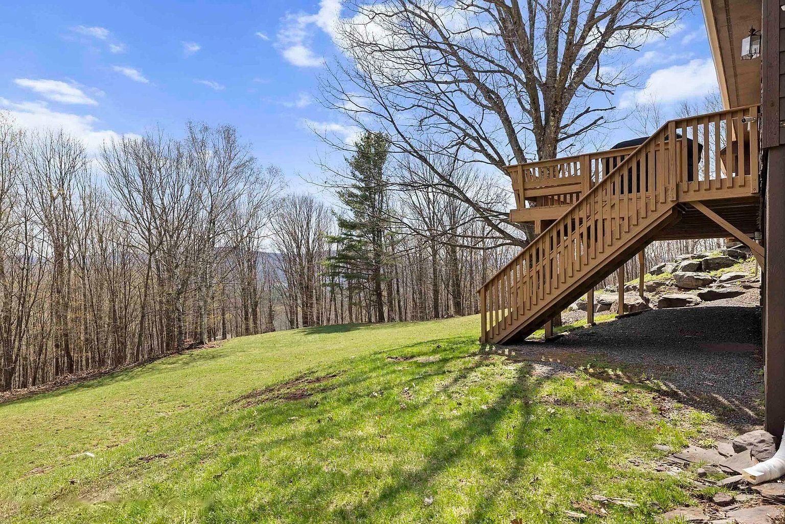 A wooden staircase leading to a building with a view of a grassy area and trees.