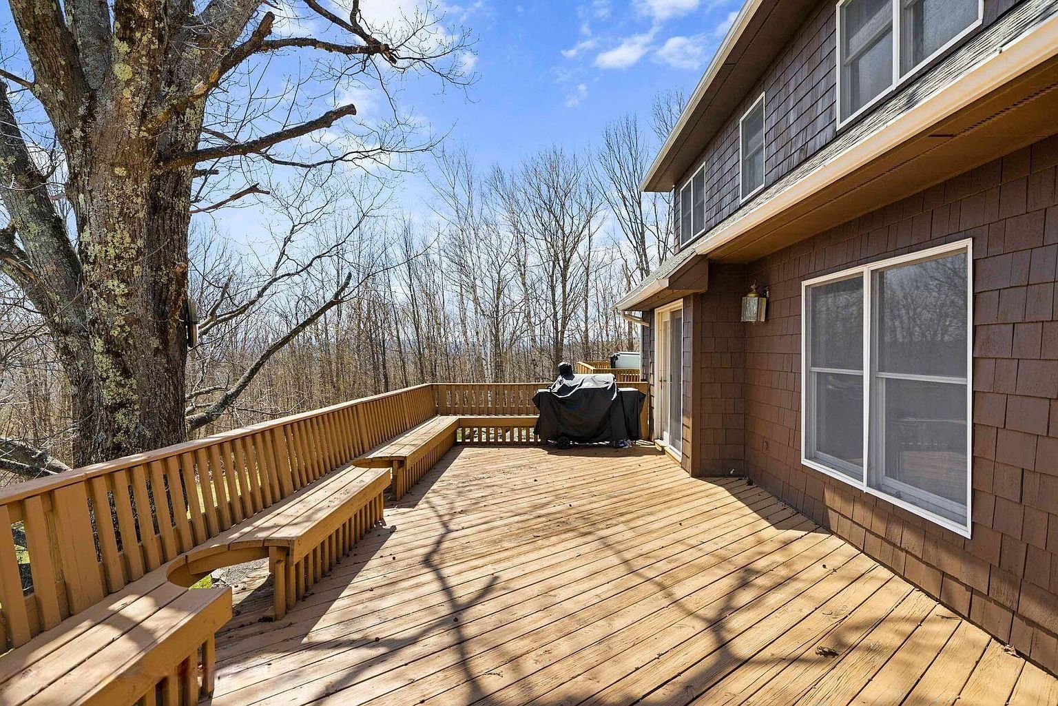 Une terrasse en bois avec des bancs, un espace barbecue couvert et une maison dotée de grandes fenêtres.