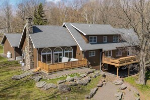 A two-story house with a stone chimney, large windows, and a wooden deck.