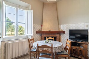 Ein Essbereich mit einem runden Tisch, Stühlen, einem Kamin, einem Fernseher und einem Fenster mit Blick auf Bäume.