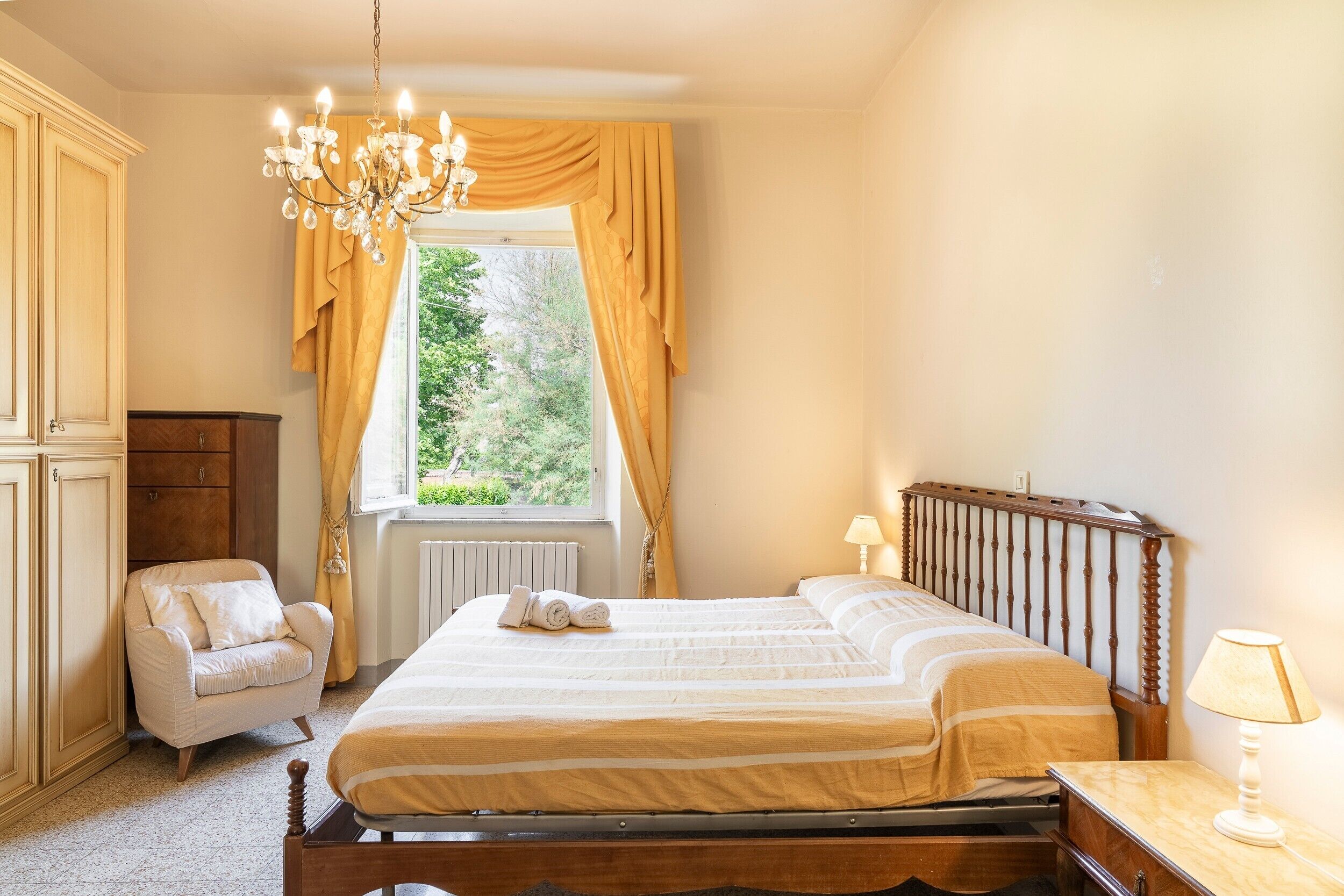 Ein Schlafzimmer mit einem Bett, einem Sessel, einem Fenster mit Vorhängen, einer Heizung und einer Deckenleuchte.