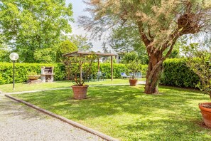 Ein gepflegter Garten mit Laube, Kübelpflanzen und Grillplatz.