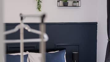 A neatly made bed with white and blue bedding, a bedside lamp, and two wall-mounted shelves with potted plants.