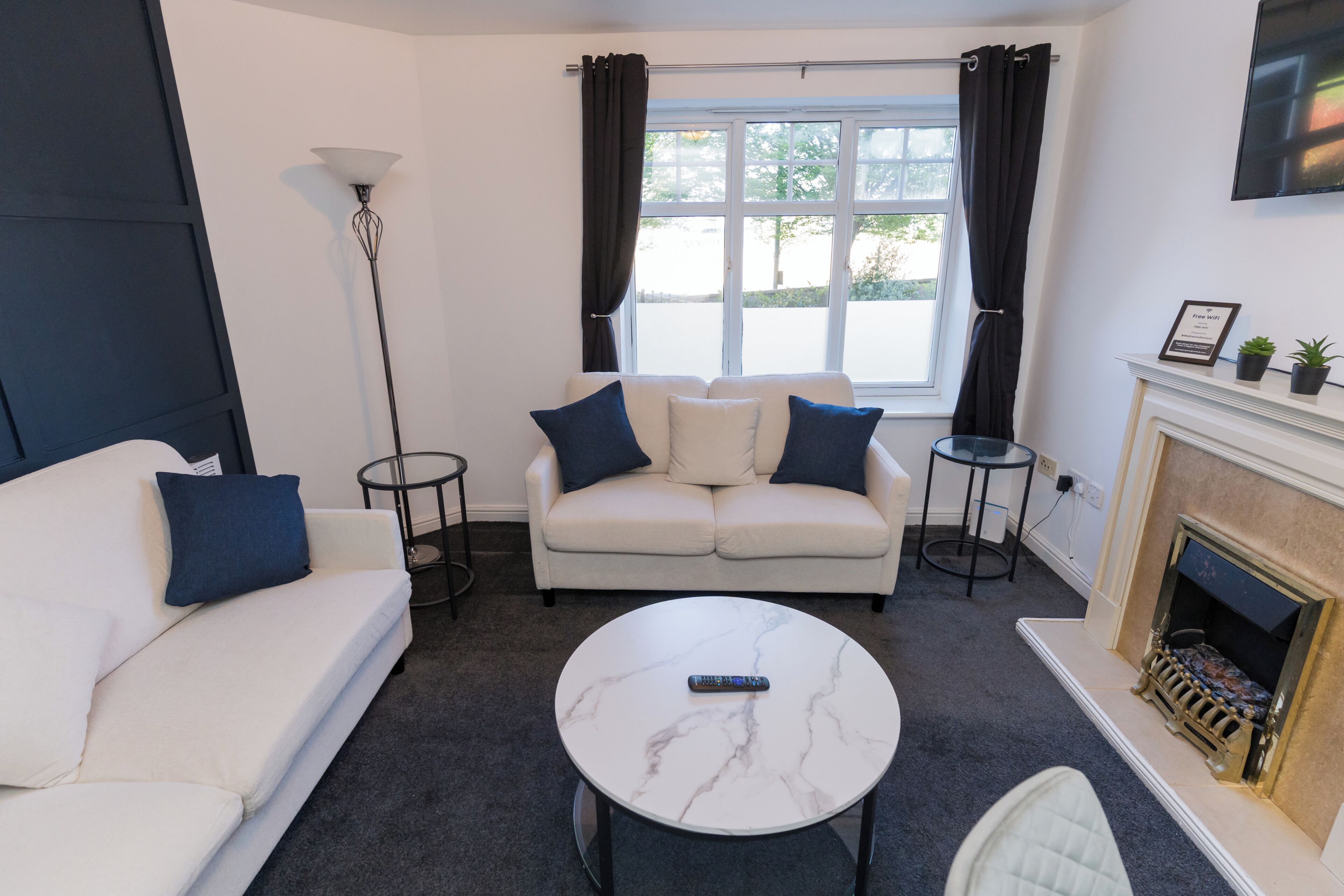 Ein Wohnzimmer mit einem weißen Sofa, einem runden Marmor-Couchtisch, einem Kamin und einem an der Wand befestigten Fernseher.