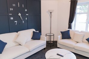 A modern living room with two white sofas, a round coffee table, a floor lamp, and a wall clock. - Boutique 2-Bed Apartment in Wolverhampton Centre (Wolverhampton)