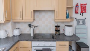 A compact kitchen with wooden cabinets, a gas stove, a built-in oven, a kettle, a toaster, a spice rack, and a fire blanket on the wall. - Boutique 2-Bed Apartment in Wolverhampton Centre (Wolverhampton)