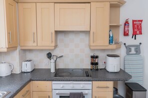 A compact kitchen with wooden cabinets, a gas stove, a built-in oven, a kettle, a toaster, a spice rack, and a fire blanket on the wall. - Boutique 2-Bed Apartment in Wolverhampton Centre (Wolverhampton)
