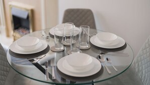 A round glass table set for four with white plates, clear glasses, and silverware. - Boutique 2-Bed Apartment in Wolverhampton Centre (Wolverhampton)