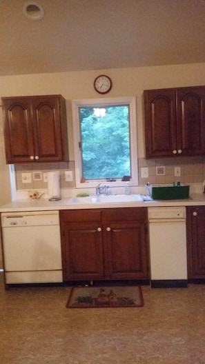 A kitchen with wooden cabinets, a window, a sink, and a clock on the wall. - Cozy 2-bedroom house in welcoming Spring Lake with AC (Spring Lake)