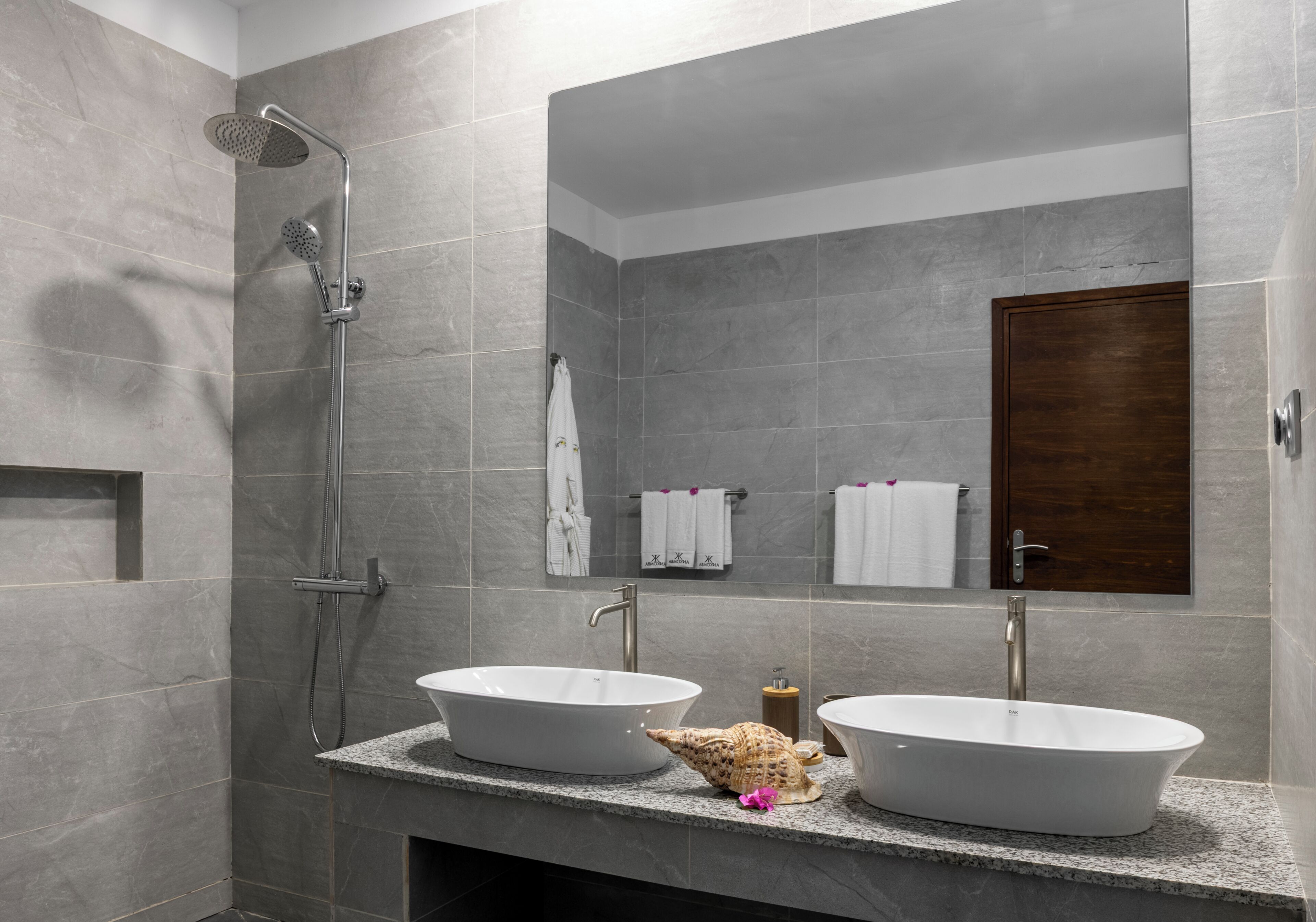 Un baño moderno con dos lavamanos, ducha y puerta de madera.