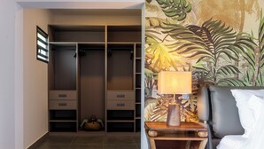 A bedroom with a bed, a nightstand, a lamp, a closet with shelves, and a wall with a leaf pattern. - Ankomba Hotel (Nosy Komba)