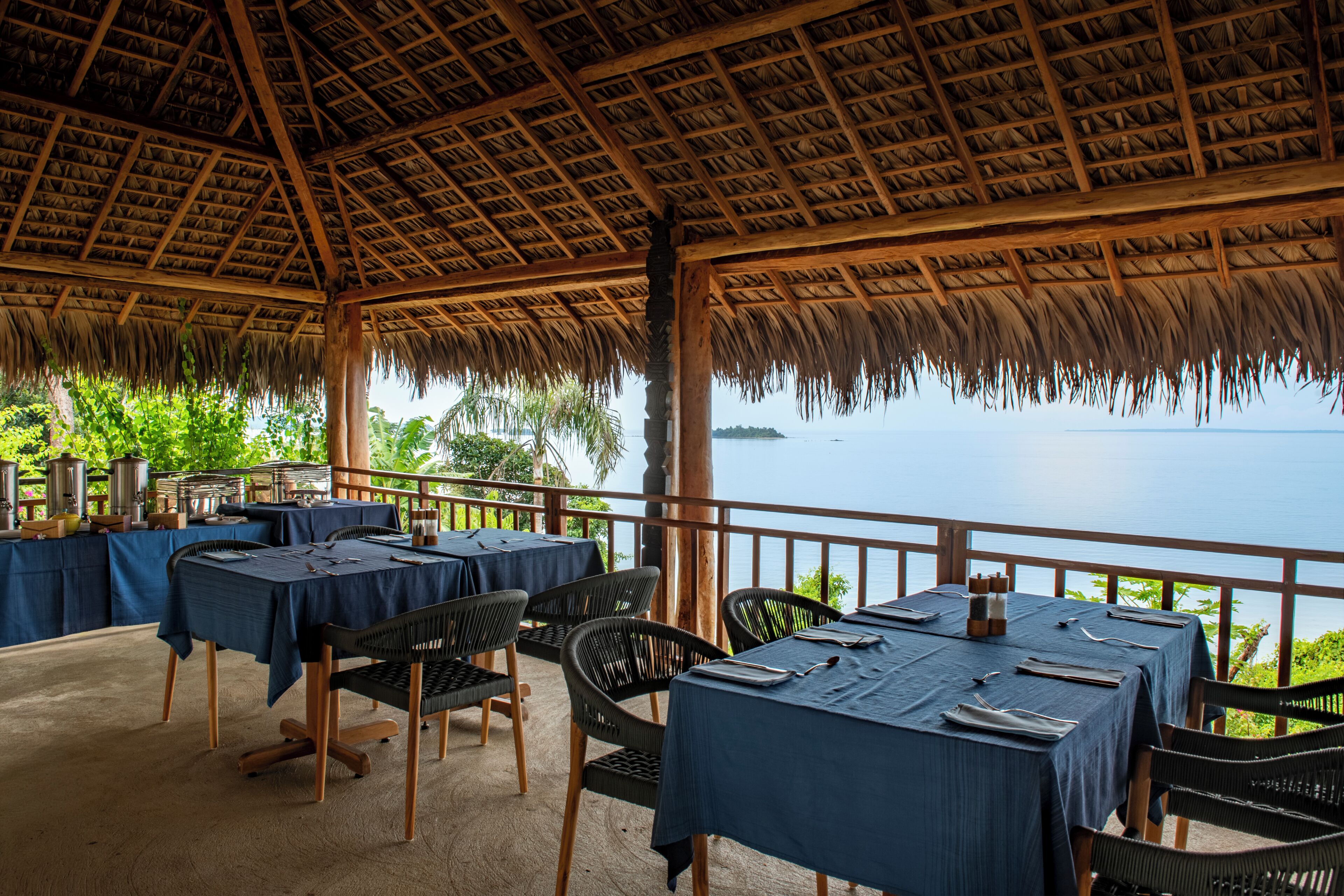 Un área de comedor al aire libre con mesas y sillas, con vista a un cuerpo de agua.