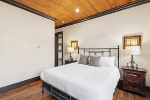 Ein Schlafzimmer mit Holzboden, einem Bett mit weißer Bettwäsche, zwei Nachttischen mit Lampen und einem Schminktisch mit Schublade.