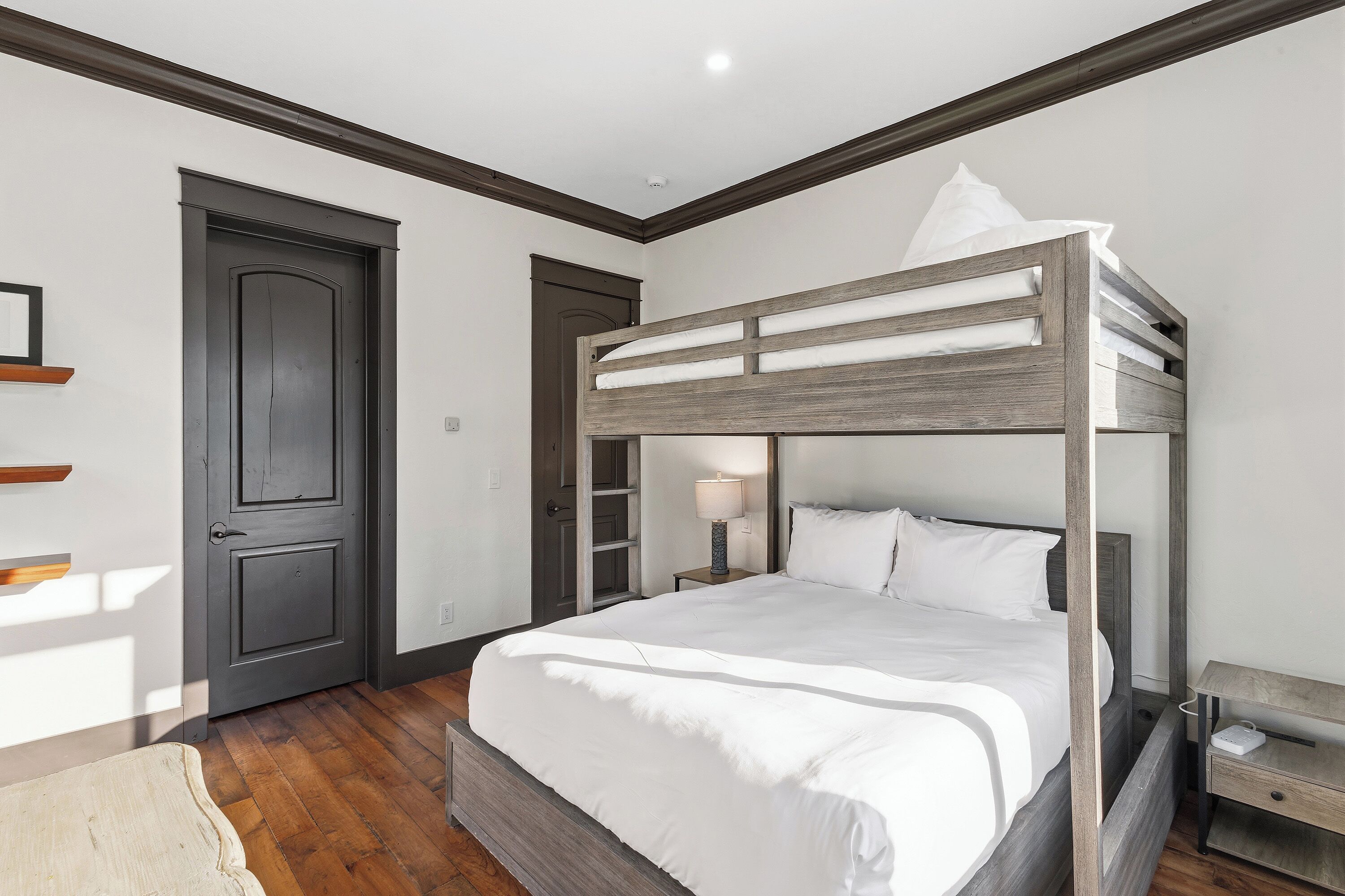 A bunk bed with white bedding in a room with wooden flooring and dark walls.