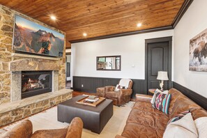Ein gemütliches Wohnzimmer mit Kamin aus Stein, Ledersofas und einem Wand-Fernseher.