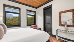 Una camera da letto con un letto grande, una cassettiera, uno specchio e due finestre con vista sulle montagne.