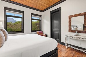 Ein Schlafzimmer mit einem großen Bett, einem Schminktisch, einem Spiegel und zwei Fenstern mit Bergblick.
