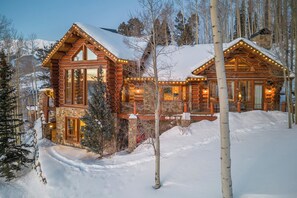 Eine Blockhütte mit Steinuntergrund, großen Fenstern und einem mit Schnee bedeckten Dach.