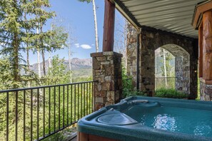 Una vasca idromassaggio su un portico con pareti in pietra e vista sulle montagne.