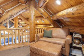 Ein rustikales Blockhaus mit Ledersofa, Hocker und einer Holztreppe.