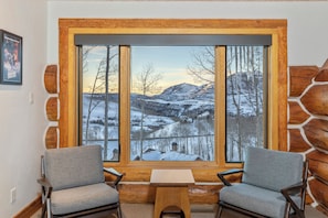 Una habitación con un ventanal que ofrece vistas a un paisaje nevado, dos sillas y una pequeña mesa.