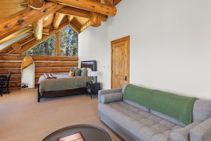Un dormitorio tipo cabaña de madera con una cama, un sofá, un escritorio y un ventanal grande.