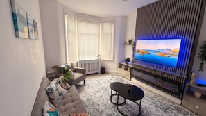 A modern living room with a sofa, a coffee table, a flat-screen TV, and a fireplace. - Stylish 3BR House in Newham East London&Hot Tub (London)