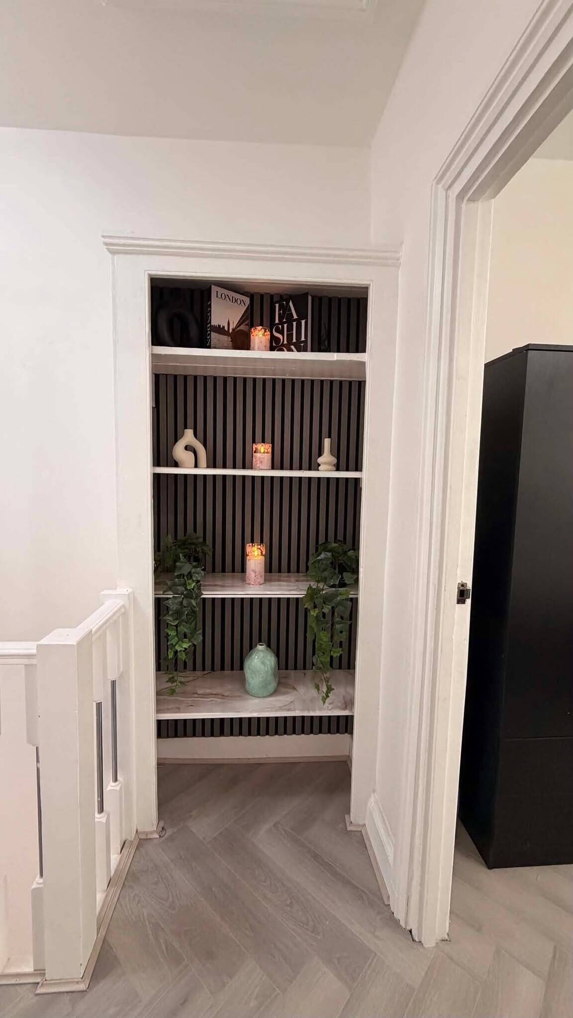 A hallway with a white door, a black door, and a shelf with decorative items.