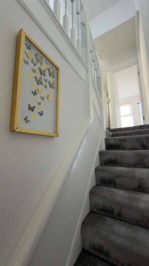 A staircase with a carpeted handrail and a wall-mounted picture frame with butterflies. - Stylish 3BR House in Newham East London&Hot Tub (London)