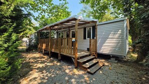 A wooden deck with a covered area, a gravel path, and a mobile home with a white exterior. - Lou Cigalou - Mobile Home - Sleeps 6 (La Roque-d'Anthéron)