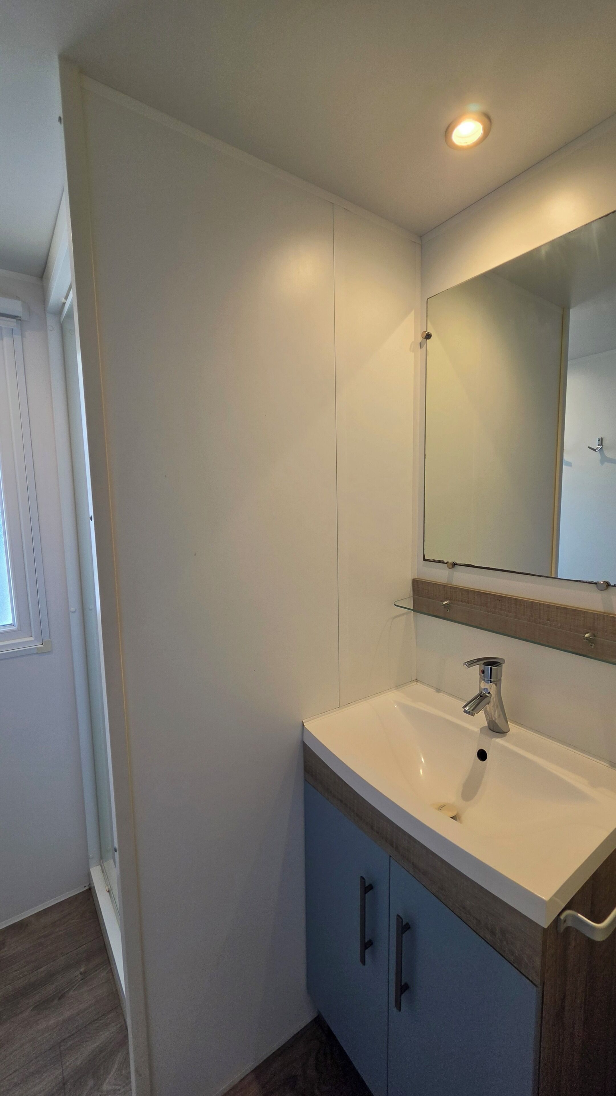 Ein Badezimmer mit einem weißen Waschbecken, einem Spiegel und einem Holzkabinent.