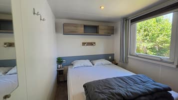 Ein Schlafzimmer mit einem Bett, einem Nachttisch, einem Spiegel, einem Fenster mit Vorhängen und einem an der Wand befestigten Regal.