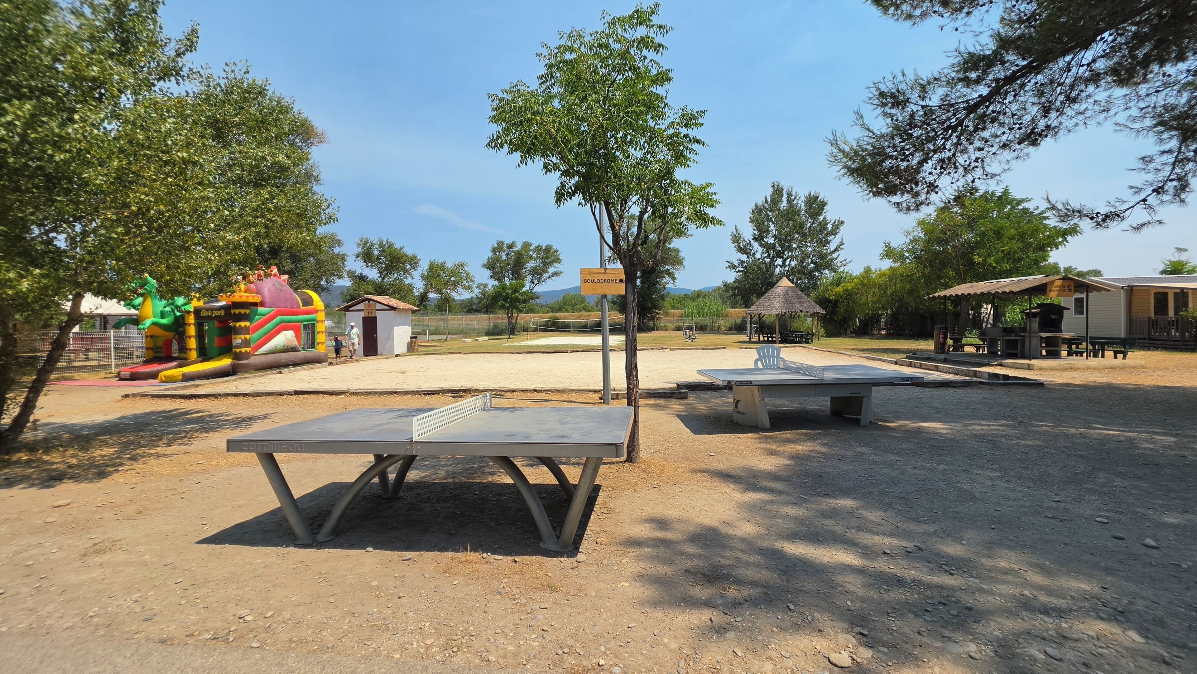 An outdoor recreational area with a ping pong table, a small building, and a dinosaur-themed play structure.