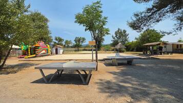 An outdoor recreational area with a ping pong table, a small building, and a dinosaur-themed play structure.