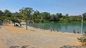 A lakeside area with a gravel beach, lounge chairs, and a clear view of the water. - Lou Cigalou - Mobile Home - Sleeps 6 (La Roque-d'Anthéron)