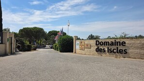A paved entrance to Domaine des Iscles with a stone wall and a sign. - Lou Cigalou - Mobile Home - Sleeps 6 (La Roque-d'Anthéron)