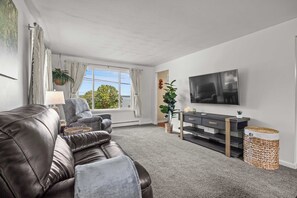 Ein Wohnzimmer mit einer Ledersofa, einem an der Wand montierten Fernseher und Blick ins Freie.