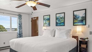 Habitación de hotel con una cama grande, un ventilador de techo, una ventana con cortinas y tres cuadros de paisajes en la pared.
