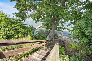 Eine Holztreppe führt zu einem Steg über dem Wasser, umgeben von Bäumen und viel Grün.